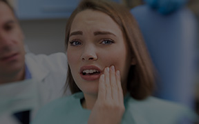 Woman in dental chair holding her jaw in pain