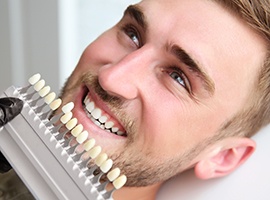 Cosmetic dentist holding tooth color chart to man's smile before teeth whitening in Brick