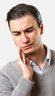 Man in beige sweater holding his jaw in pain